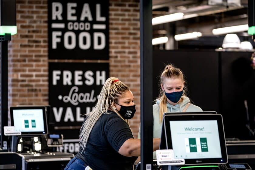 An employee assists a customer at the self-checkout lane during the grand opening of Fresh Thyme Market
