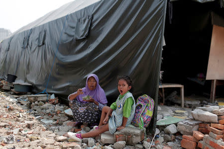 A child and her mother sit near their temporary shelter after their houses were demolished last year, in Luar Batang area in Jakarta, Indonesia April 18, 2017. REUTERS/Beawiharta