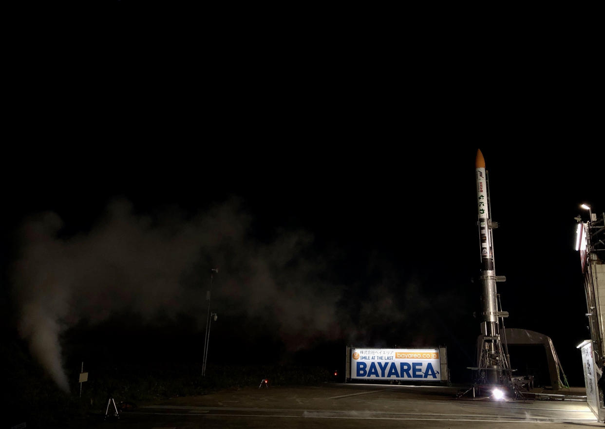  a small white rocket stands on a launch pad at night. 