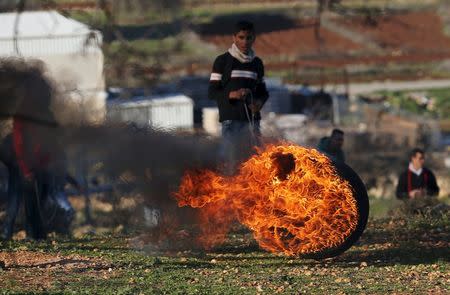 A Palestinian protester stands behind a burning tyre during clashes with Israeli troops, near Israel's Ofer Prison near the West Bank city of Ramallah December 25, 2015. REUTERS/Mohamad Torokman