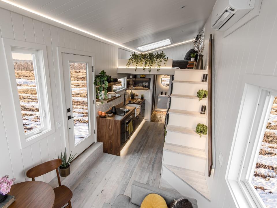 a wide angle view of the tiny home's staircase, loft, kitchen, windows, and entry door