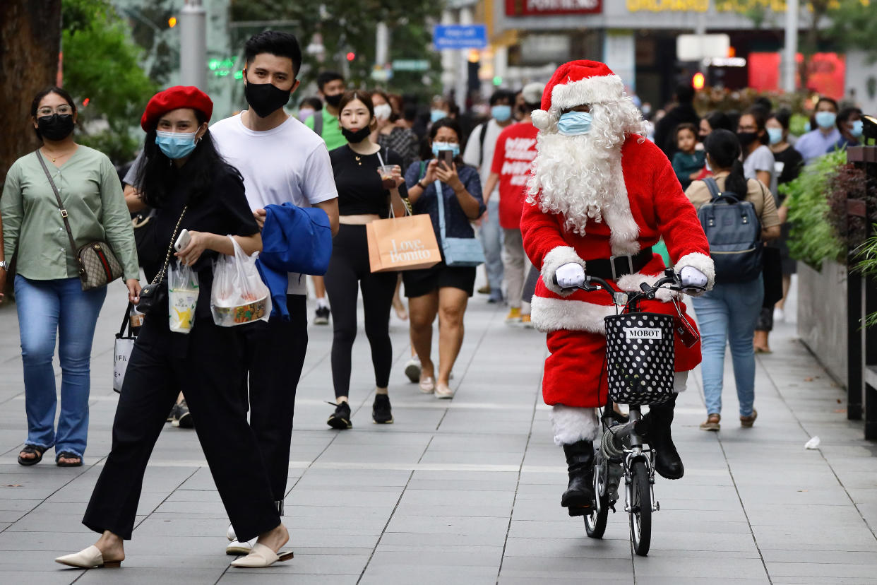 SINGAPORE - DECEMBER 24: A man dressed as Santa Claus wears a protective mask as he rides and greets shoppers along the Orchard Road shopping belt on December 24, 2020 in Singapore. As Singapore prepares to further ease COVID-19 restrictions from December 28, the government reported its first COVID-19 case carrying the potentially more contagious strain of the virus circulating in the United Kingdom yesterday. As of 24 December, the Ministry of Health confirmed 13 new imported COVID-19 cases in the wider community bringing the country's total to 58,495. (Photo by Suhaimi Abdullah/Getty Images)