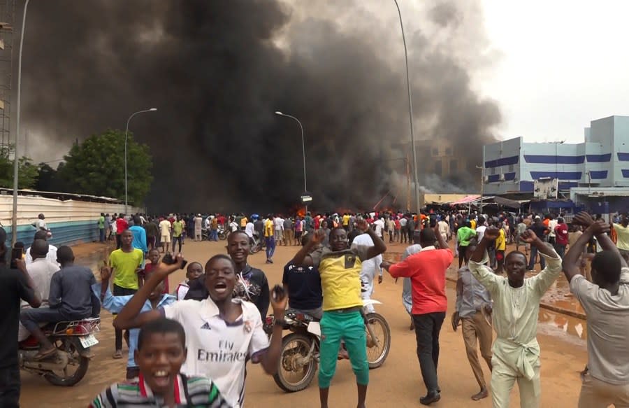 With the headquarters of the ruling party burning in the back, supporters of mutinous soldiers demonstrate in Niamey, Niger, Thursday, July 27 2023. (AP Photo/Fatahoulaye Hassane Midou)