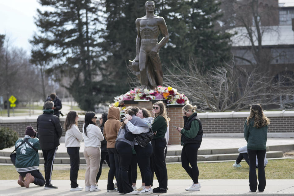 Students gather where flowers are being left at the Spartan Statue on the grounds of Michigan State University, in East Lansing, Mich., Tuesday, Feb. 14, 2023. A gunman killed several people and wounded others at Michigan State University. Police said early Tuesday that the shooter eventually killed himself. (AP Photo/Paul Sancya)