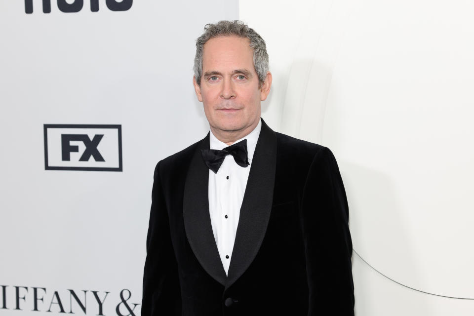 tom in a black tuxedo with a bow tie standing in front of a promotional backdrop