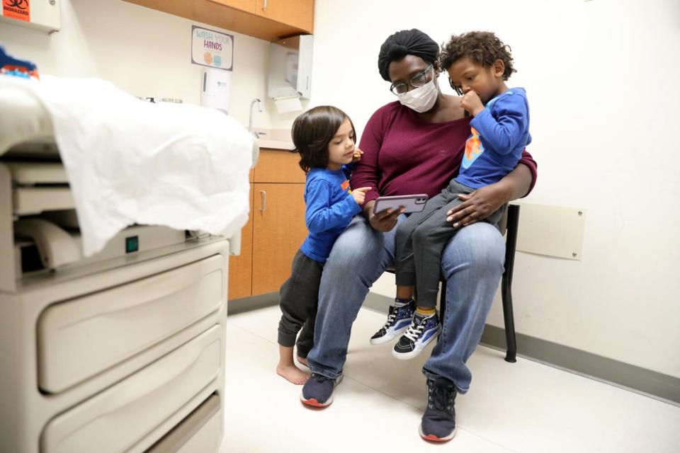 A woman waits with two children in a doctor's office.