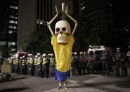 Military policemen stand in a line behind a demonstrator wearing the figure of a skeleton holding up a trophy representing that of the FIFA World Cup during a protest against the 2014 World Cup, in Sao Paulo May, 15 2014. Road blocks and marches hit Brazilian cities on Thursday as disparate groups criticized spending on the upcoming World Cup soccer tournament and sought to revive a call for better public services that swept the country last June. REUTERS/Nacho Doce (BRAZIL - Tags: SPORT SOCCER CIVIL UNREST WORLD CUP TPX IMAGES OF THE DAY)