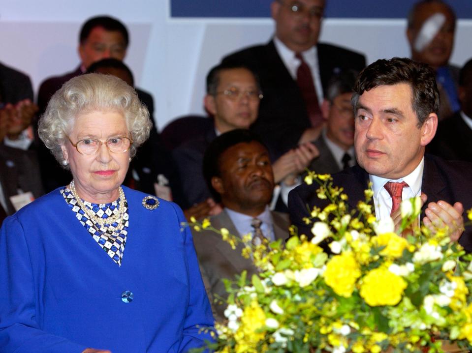 Queen Elizabeth and Gordon Brown in 2002 sitting in front of flowers