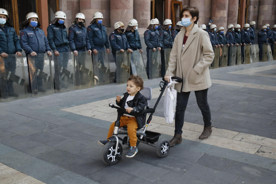 A woman wheels a stroller with a child as police officers guard in front of the government building in Yerevan, Armenia, Tuesday, Nov. 10, 2020. Some thousands of people streamed to the main square in the Armenian capital early Tuesday to protest the agreement to halt fighting over the Nagorno-Karabakh region, many shouting "We won't give up our land." Some of them broke into the main government building, saying they were searching for Pashinian, who apparently had already departed. (AP Photo/Dmitri Lovetsky)