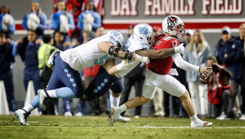 N.C. State quarterback Devin Leary (13) is sacked by North Carolina’s Tomon Fox (12) and Raymond Vohasek (51) during the first half of N.C. State’s game against UNC at Carter-Finley Stadium in Raleigh, N.C., Friday, November 26, 2021.