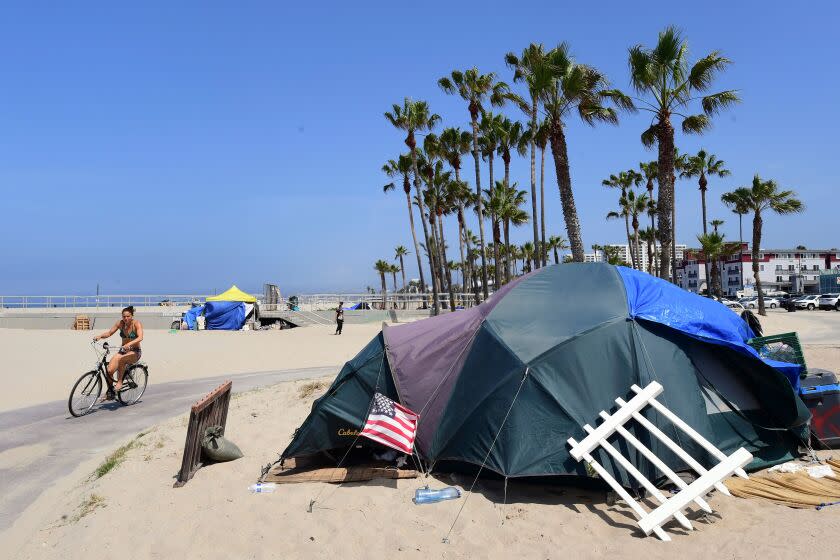 A woman cycles past a homeless encampment at Venice Beach, on June 30, 2021 in Venice, California, where an initiative began this week offering people in homeless encampments a voluntary path to permanent housing. - Homeless encampments at the famed Venice Beach has grown during the coronavirus pandemic, turning into a political flashpoint, with signs posted on trees warning of a July 2 clearance of all homeless encampments ahead of the July 4th weekend. (Photo by Frederic J. BROWN / AFP) (Photo by FREDERIC J. BROWN/AFP via Getty Images)