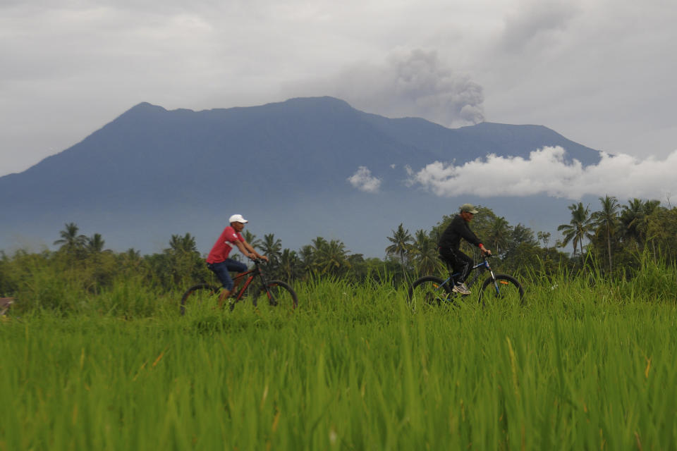 Cyclists ride past by as Mount Marapi spews volcanic material into the air in Agam, West Sumatra, Indonesia, Wednesday, Dec. 6, 2023. Rescuers were searching for a female hiker who was caught by a surprise weekend eruption of the volcano that killed nearly two dozens climbers and injured several others, officials said Wednesday. (AP Photo/Ardhy Fenando)