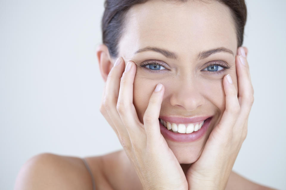 A photo of a woman smiling with her hands touching her face