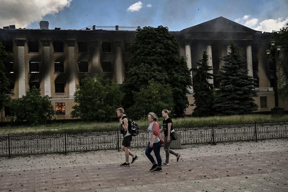 Local residents walk past a burning college after a strike in Lysychansk, eastern Ukrainian region of Donbas on 7 June (AFP via Getty Images)