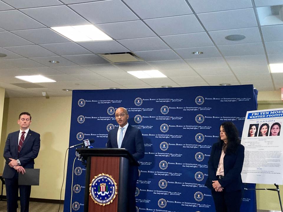 Three people stand in front of an FBI backdrop and podium, next to a "FBI Ten Most Wanted" poster.