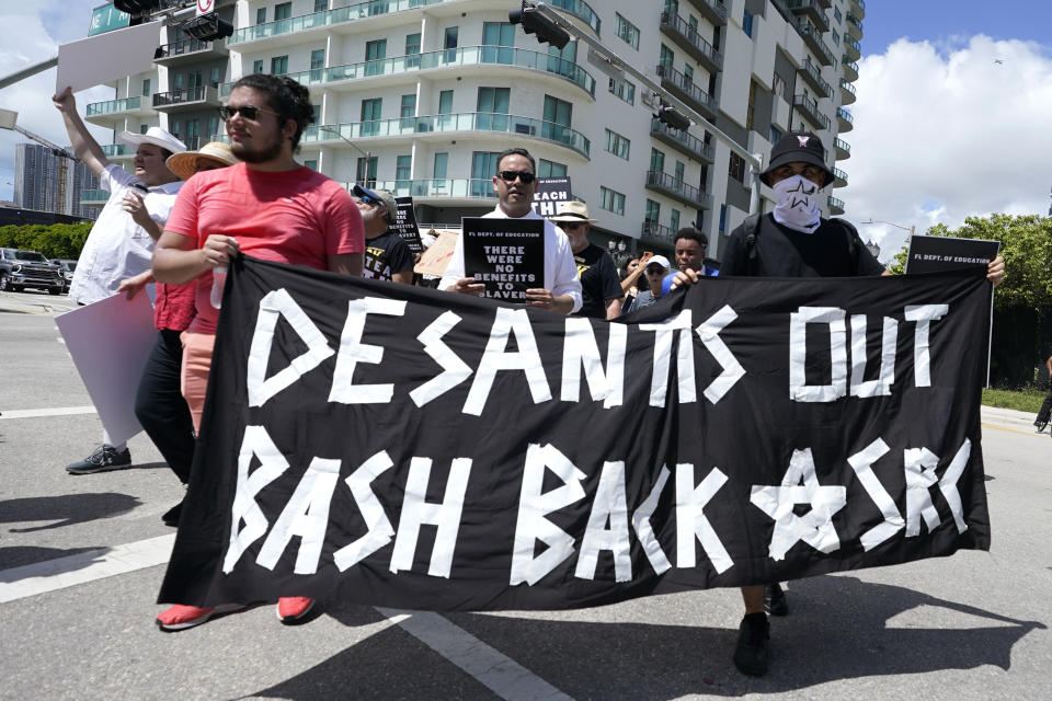 People carry a sign in reference to Florida Gov. Ron DeSantis during the "Teach No Lies" march to the School Board of Miami-Dade County to protest Florida's new standards for teaching Black history, which have come under intense criticism for what they say about slavery, Wednesday, Aug. 16, 2023, in Miami. (AP Photo/Lynne Sladky)