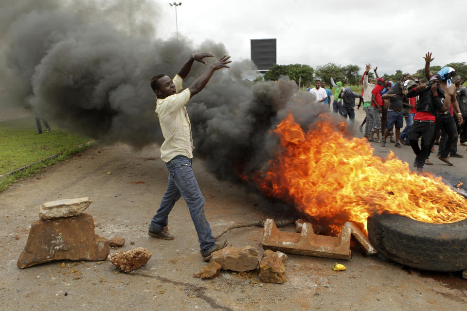 Protestors gather near a burning tire during a demonstration over the hike in fuel prices in Harare, Zimbabwe, Tuesday, Jan. 15, 2019. A Zimbabwean military helicopter on Tuesday fired tear gas at demonstrators blocking a road and burning tires in the capital on a second day of deadly protests after the government more than doubled the price of fuel in the economically shattered country. (AP Photo/Tsvangirayi Mukwazhi)