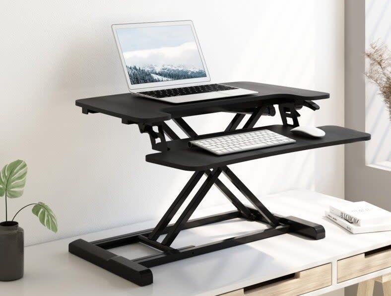 a two-tiered standing desk stand on a desk with a laptop keyboard and mouse