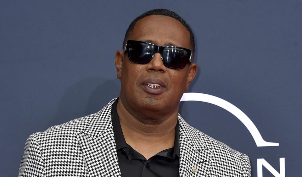 Master P poses in sunglasses and a checkered suit against a gray background.
