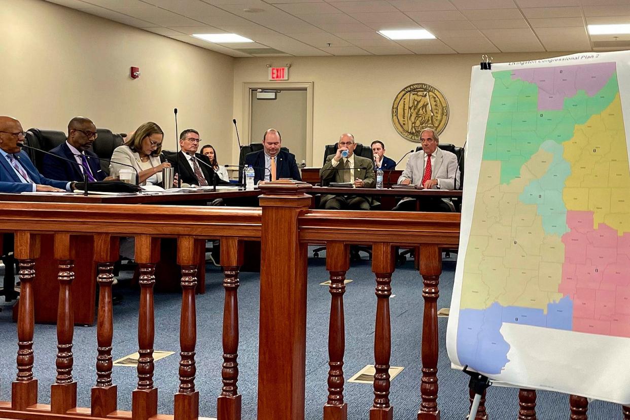 A committee sits in front of a congressional map.