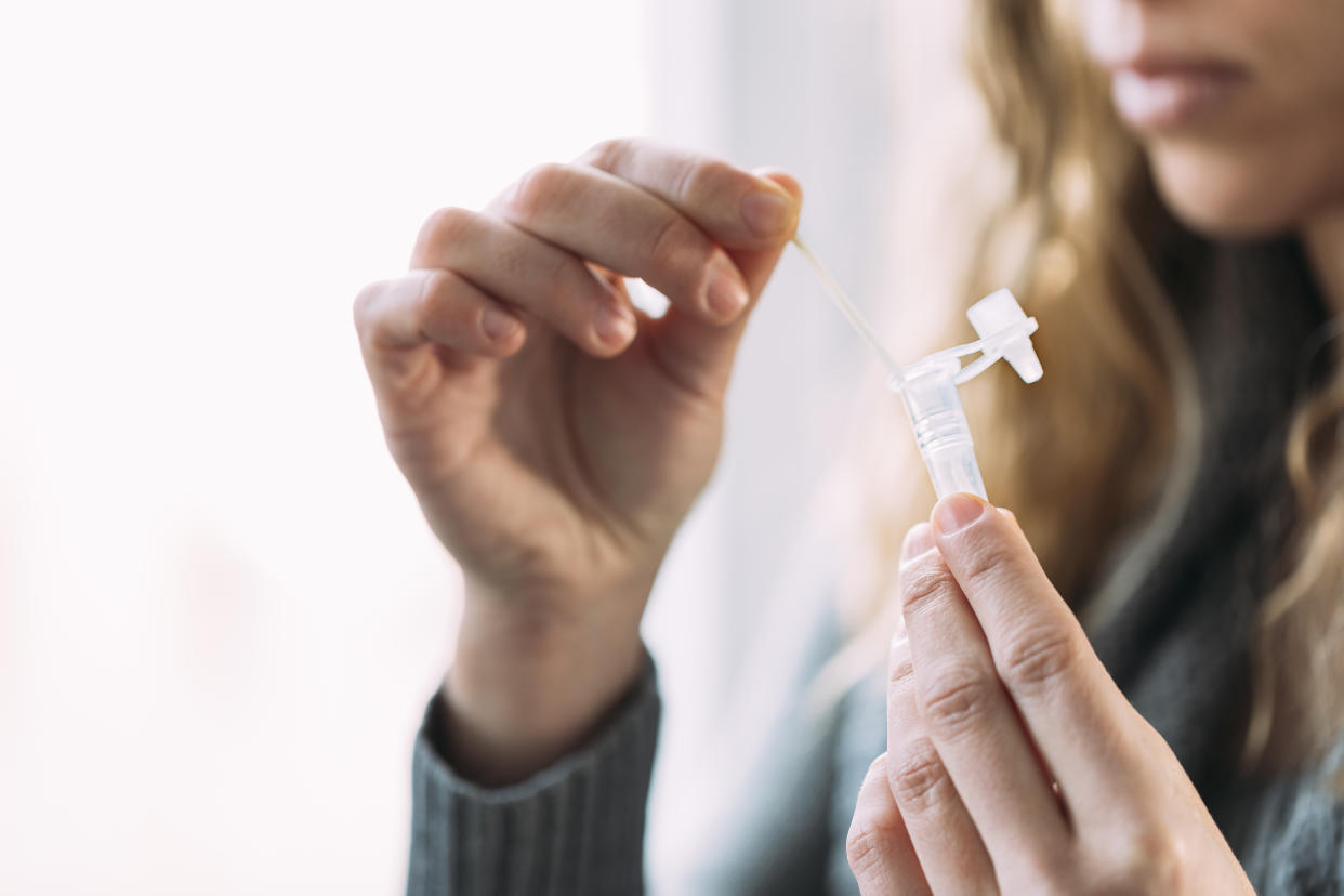 Side view of woman placing swab into the antigen test extraction tube