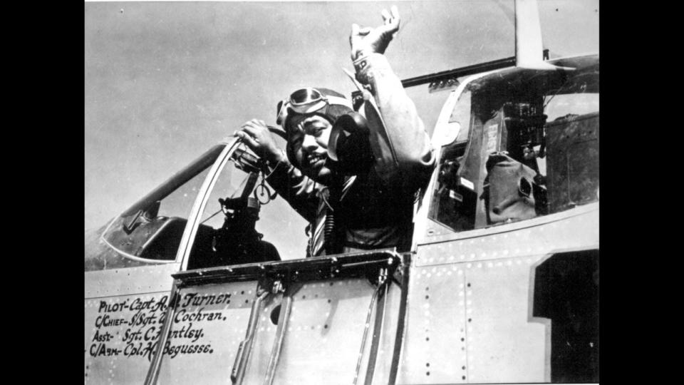 A Tuskegee Airman waves from the cockpit of an aircraft.