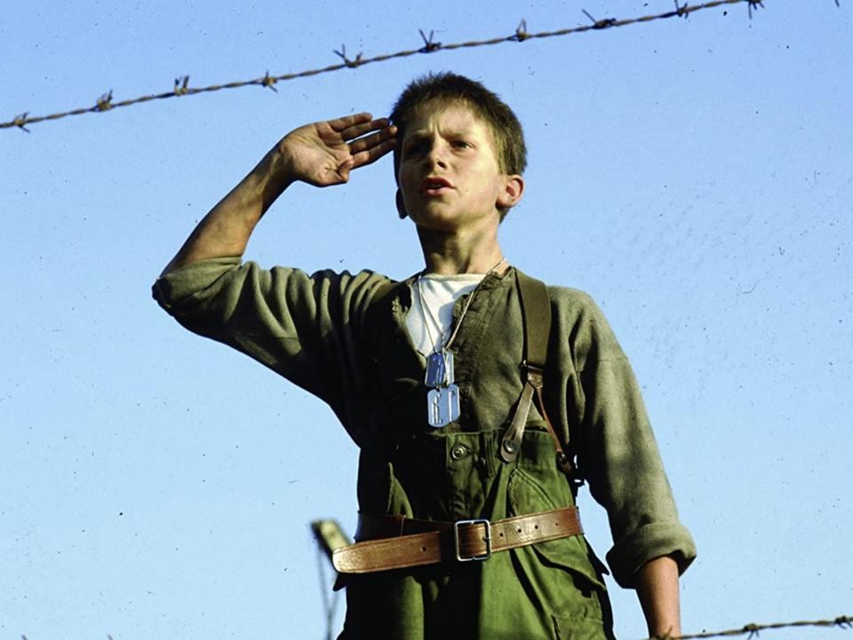 A young Christian in a green utility suit saluting in front of barbed wires.