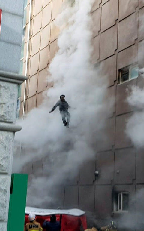 A survivor jumps down to an air mattress as he waits for rescue from a burning building in Jecheon - Credit: REUTERS