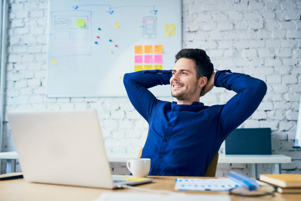 A man smiles while sitting behind a laptop.