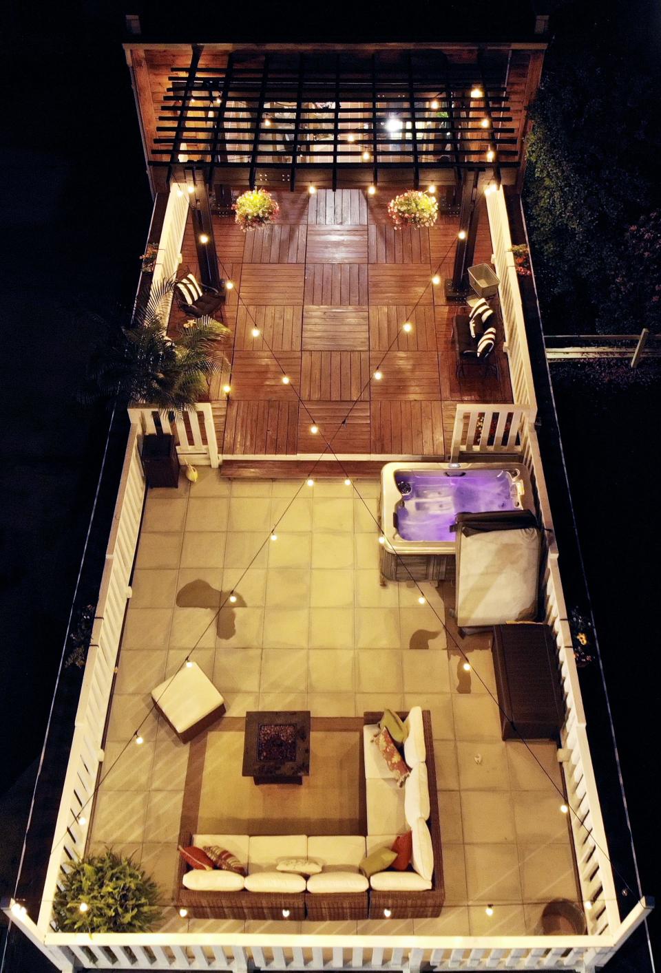 A picture of the rooftop deck. It has woodern flooring, an outdoor sofa, string lights and a hot tub