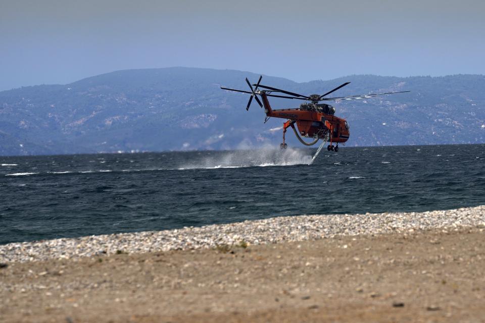 An helicopter fills water during a wildfire at Pefki village on Evia island, about 189 kilometers (118 miles) north of Athens, Greece, Monday, Aug. 9, 2021.Firefighters and residents battled a massive forest fire on Greece's second largest island for a seventh day Monday, fighting to save what they can from flames that have decimated vast tracts of pristine forest, destroyed homes and businesses and sent thousands fleeing. (AP Photo/Petros Karadjias)