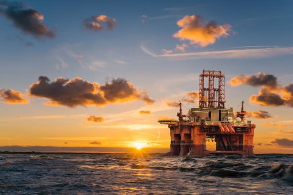 An oil rig in the middle of an ocean with the sun setting behind it.