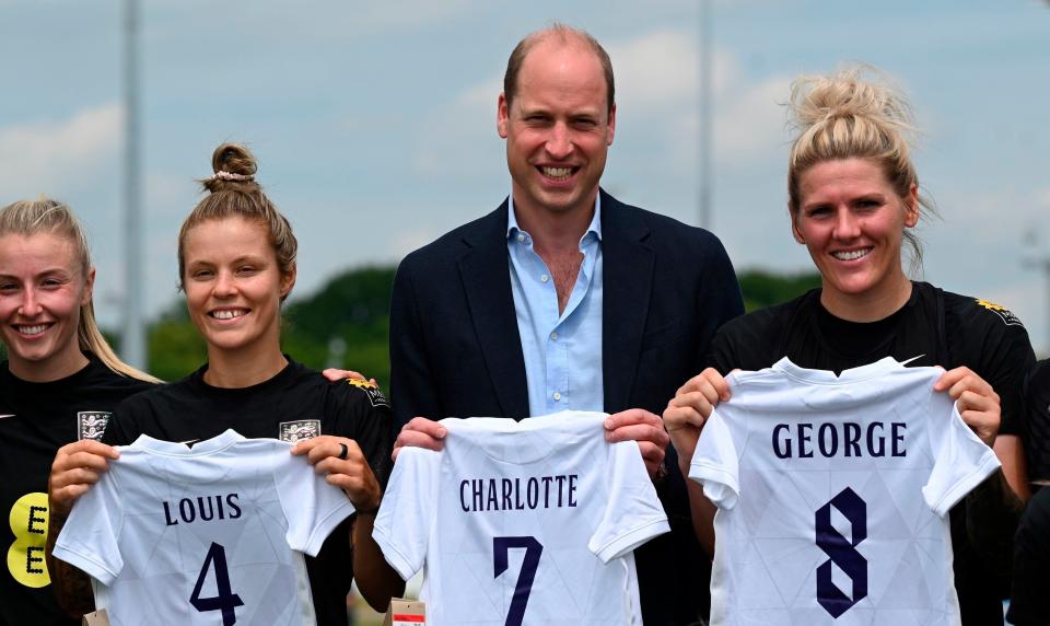 Britain's Prince William, center, holds the England football jersey bearing the names of his three children with the England women's football team during a visit to St George's Park, England's national football center in Burton-on-Trent, on June 15, 2022.