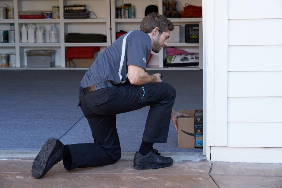 An Amazon driver sliding a package into the corner of a garage.