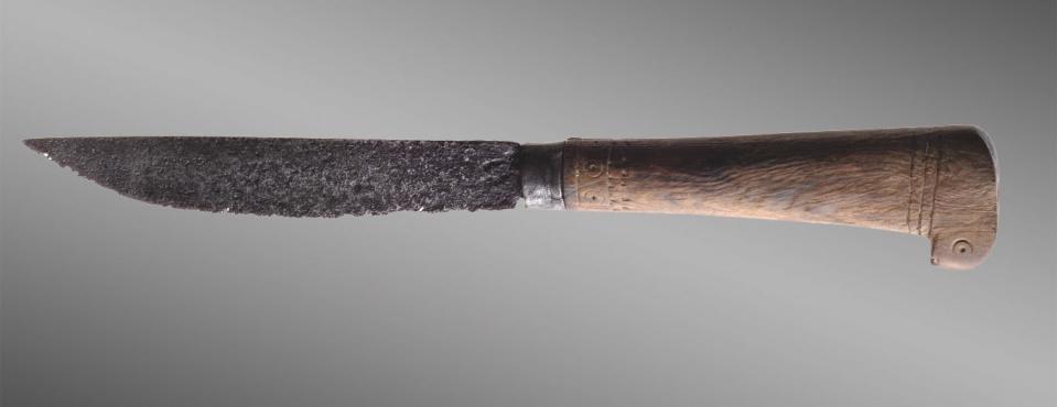 gnarled iron knife with engraved wooden handle against a grey background