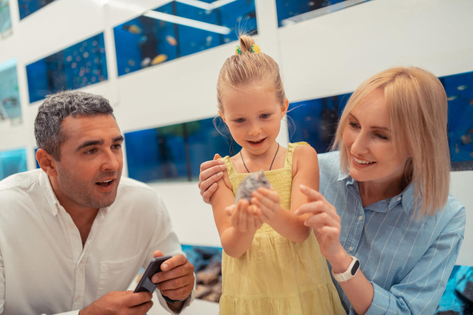 A little girl holding a small rodent as her parents look on