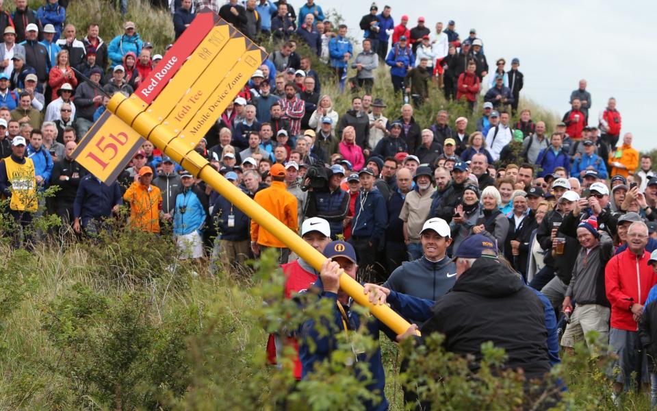 Rory McIlroy looks on as the signpost blocking the line of his second shot is removed after his errant tee shot  - Credit: Getty Images