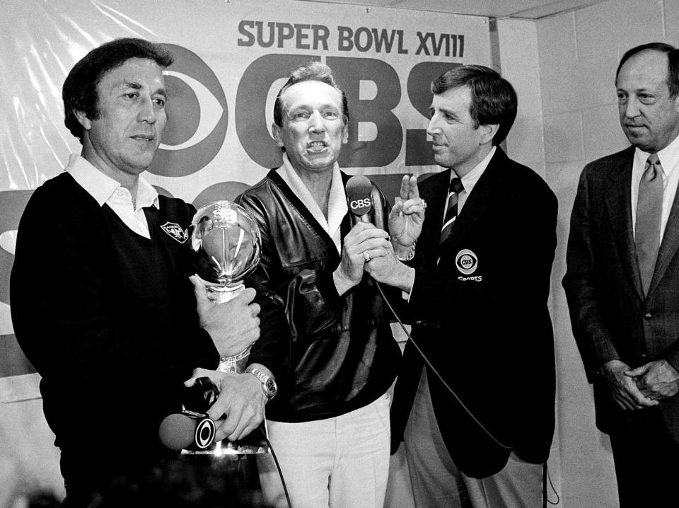 FILE - In this Jan. 23, 1984, file photo, Oakland Raiders coach Tom Flores clutches the Super Bowl trophy as Raiders managing general partner Al Davis is interviewed by Brent Musburger in the locker room after their 38-9 win over the Washington Redskins in Super Bowl XVIII in Tampa, Fla. At right is NFL Commissioner Pete Rozelle. Musburger is calling an end to his broadcast career. Millions of Americans experienced sporting events through his folksy narration, most often when he was the lead voice of CBS Sports during the 1980s. Musburger will call his last game for ESPN on Jan. 31, a college basketball contest pitting Kentucky against Georgia. (AP Photo/File)