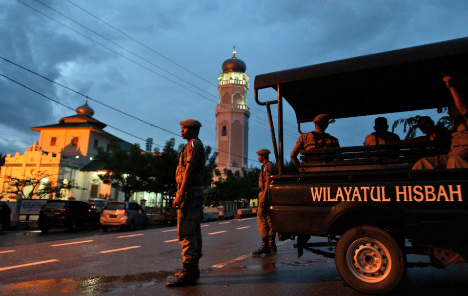 FILE - In this Dec. 31, 2013 file photo, Sharia police officers stand guard at a check point set up to prevent people from celebrating New Year's eve in Banda Aceh, Aceh Province, Indonesia. An Indonesian woman who was gang-raped by men who accused her of having extramarital sex may be caned publicly for violating Islamic law, an official said Wednesday, May 7, 2014. The 25-year-old widow said she was raped by eight men who allegedly found her having sex with a married man in her house. The men reportedly beat the man, doused the two with sewage, and then turned them over to Islamic police in conservative Aceh province, the only province in the world's most populous Muslim country that implements Islamic sharia law. New Year's celebrations are widespread in Indonesia except in Aceh, where Islamic clerics prohibit Muslims from celebrating the festivities. (AP Photo/Heri Juanda, File)