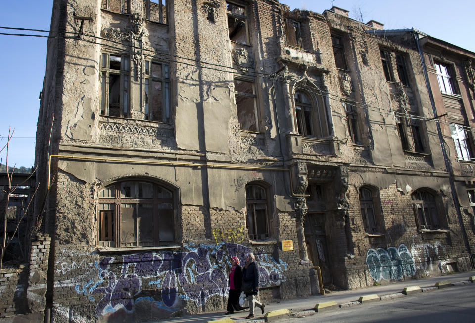 In this Sunday, March 17, 2019 photo, women walk past a war damaged building in Sarajevo, Bosnia-Herzegovina. Nearly a quarter of a century since Bosnia's devastating war ended, former Bosnian Serb leader Radovan Karadzic is set to hear the final judgment on whether he can be held criminally responsible for unleashing a wave of murder and mistreatment by his administration's forces. United Nations appeals judges on Wednesday March 20, 2019 will decide whether to uphold or overturn Karadzic's 2016 convictions for genocide, crimes against humanity and war crimes and his 40-year sentence. (AP Photo/Darko Bandic)