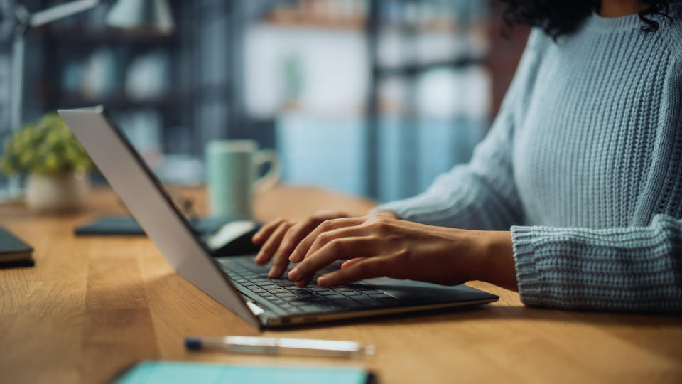 A close up of a woman sitting at a table and typing on a computer (a laptop)