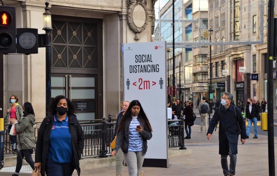 LONDON, UNITED KINGDOM - 2020/11/10: People wearing face masks as a precaution walking past a social distancing sign on Oxford Street. Most shops, restaurants and businesses have closed as the second month-long nationwide Covid 19 lockdown begins in England. (Photo by Vuk Valcic/SOPA Images/LightRocket via Getty Images)