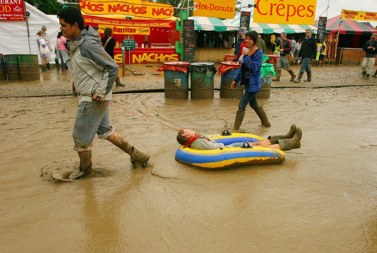 A festival attendee pulling friend through the mud on an inflatable dingy in 2005 (Getty Images)