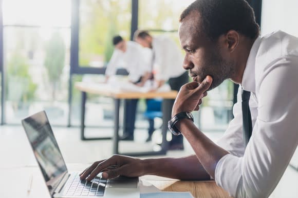 A man in a shirt and tie looking at a laptop