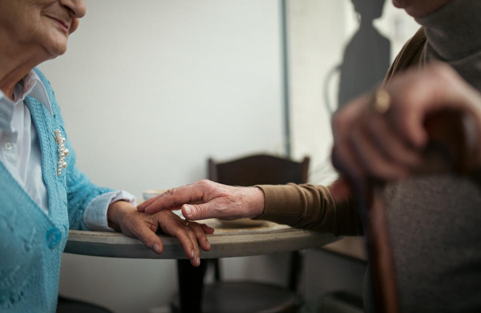 Midsection of older elegant man touching older woman's hand in café.