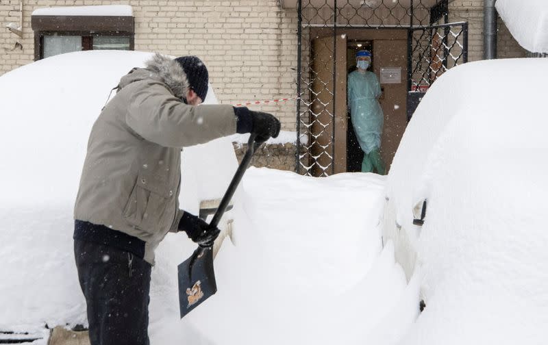 A medical specialist looks out of a dentist's clinic as a man removes snow in a street in Moscow