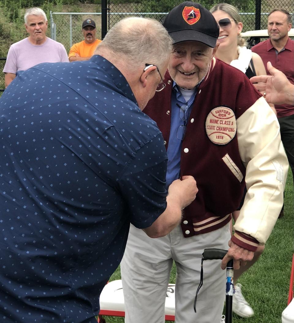 With some help from Paul Auger, John Cochin slips into his old high school athletic jacket during the ceremony at which a Sanford High School baseball field was dedicated to him on July 14, 2023.