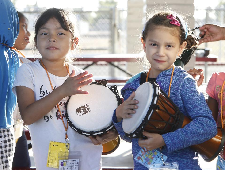 Students Maryori Molina Quinonez, left, and Kritza Ardon Blanco, right, pose for a picture as they drum in music class at Valencia Newcomer School Thursday, Oct. 17, 2019, in Phoenix. Children from around the world are learning the English skills and American classroom customs they need to succeed at so-called newcomer schools. Valencia Newcomer School in Phoenix is among a handful of such public schools in the United States dedicated exclusively to helping some of the thousands of children who arrive in the country annually. (AP Photo/Ross D. Franklin)