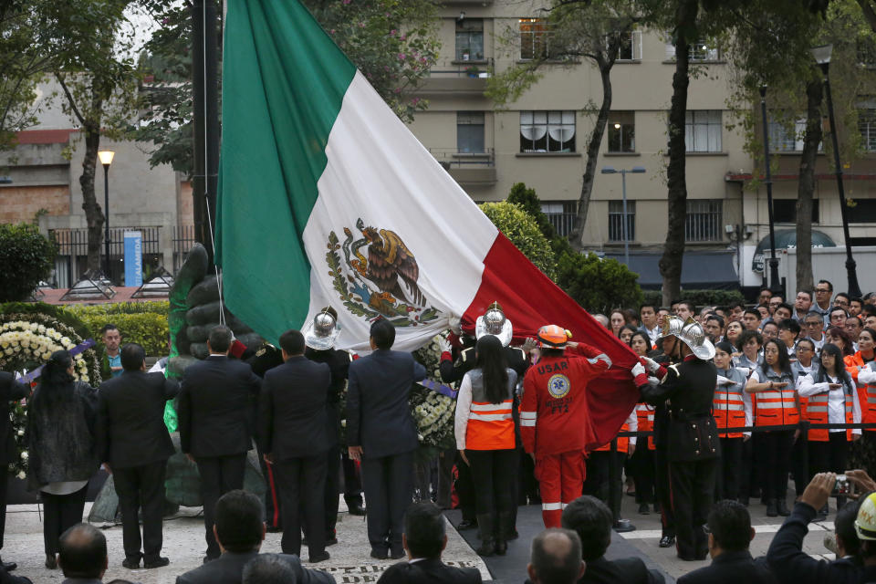 Firefighters and rescue workers stand before a Mexican national flag in front of a 1985 earthquake memorial marking that quake's 33rd anniversary and last year's 7.1 magnitude earthquake, in Mexico City, Wednesday, Sept. 19, 2018. The rescue workers, known as "topos," are a voluntary civil brigade, who were created during the 1985 earthquake that left at least 9,500 dead. (AP Photo/Marco Ugarte)