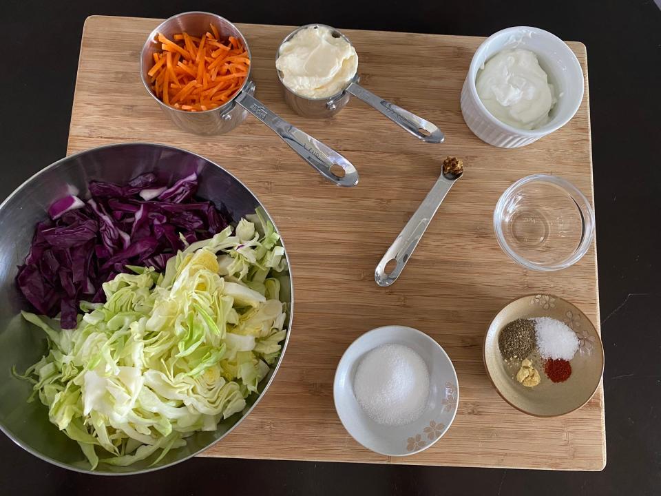 Shredded cabbage, carrots, mayonnaise, and spices and herbs in bowls on a wooden tray.